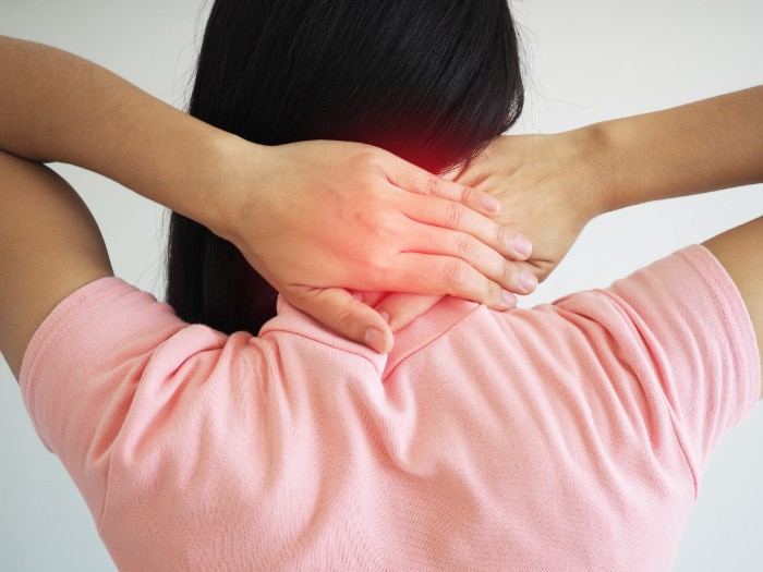 Mulher de costas com as mãos na nuca e um ponto vermelho ilustrando a intensa dor cervical, sintoma clássico de quem sofre com um nervo do pescoço inflamado.