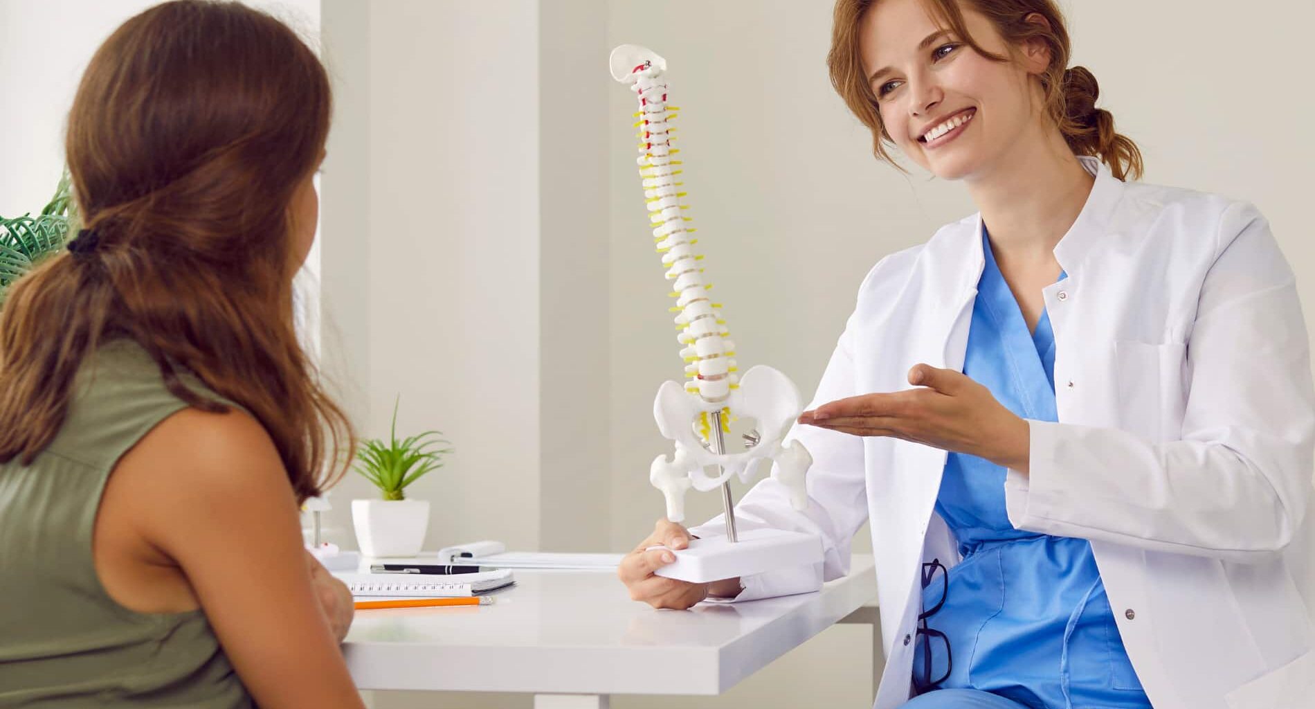 Uma médica especialista explicando um tratamento de coluna conservador para uma paciente, usando um modelo de coluna vertebral.